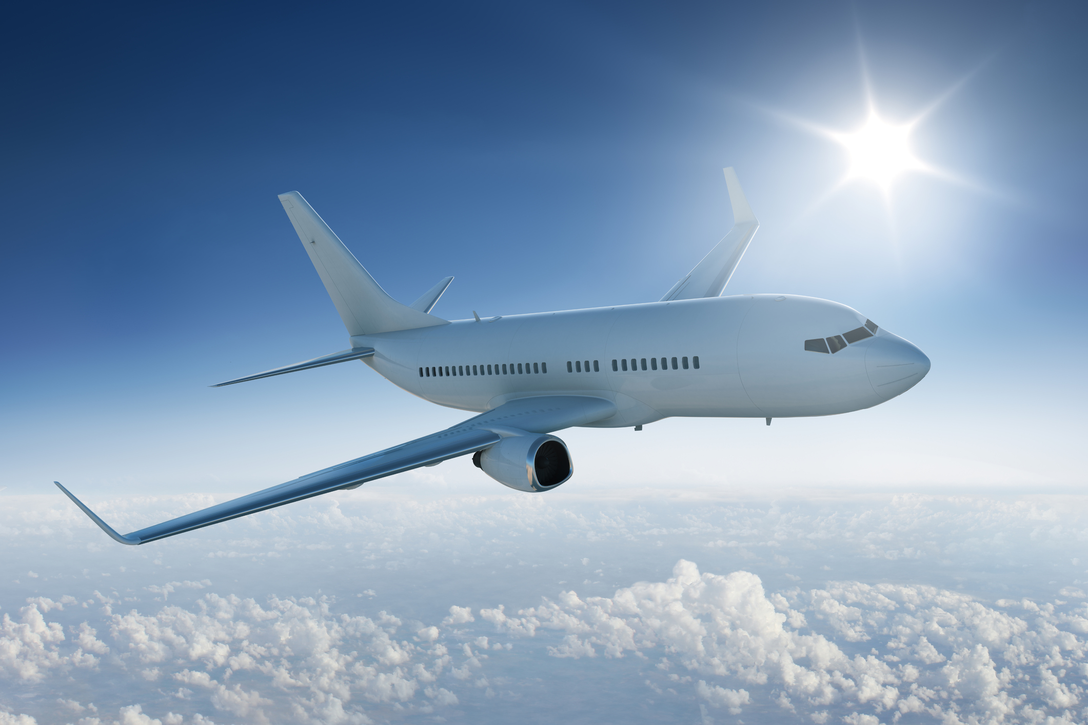 Airplane flies above the clouds in blue sky with sun in background.